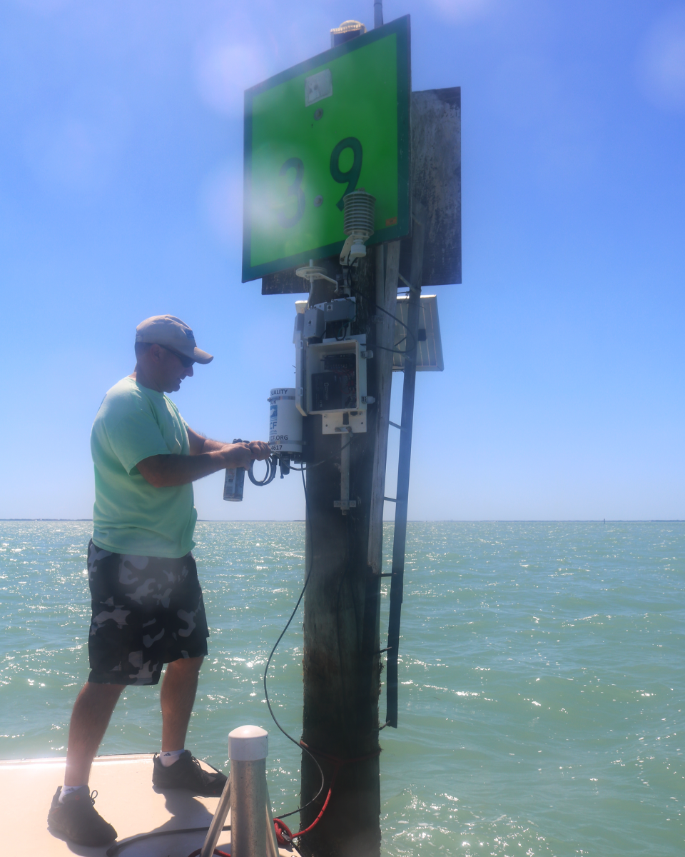 A man in a ball cap and shorts pulls a piece of equipment out of the water on the edge of a dock.